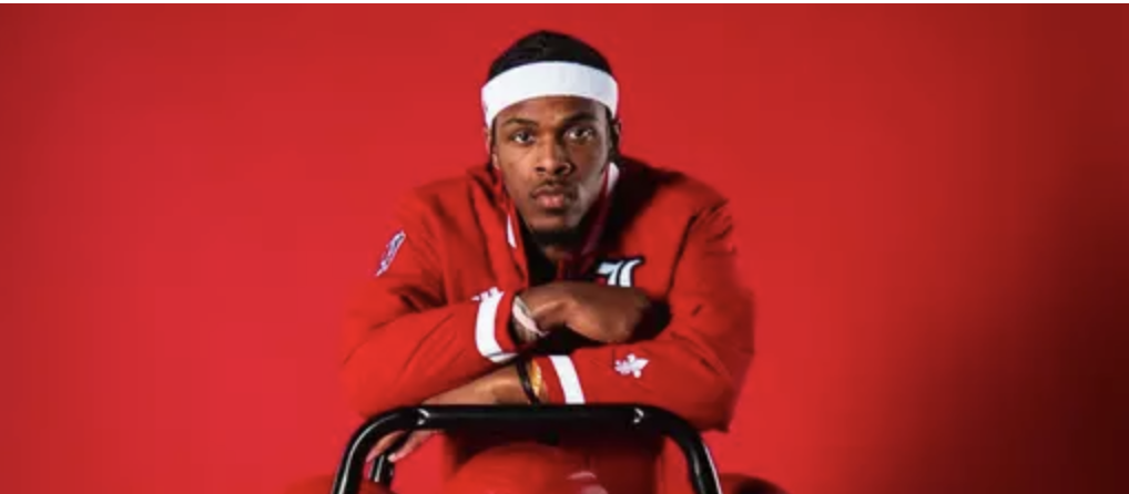 Ryan Conwell before a red background leaning on ball