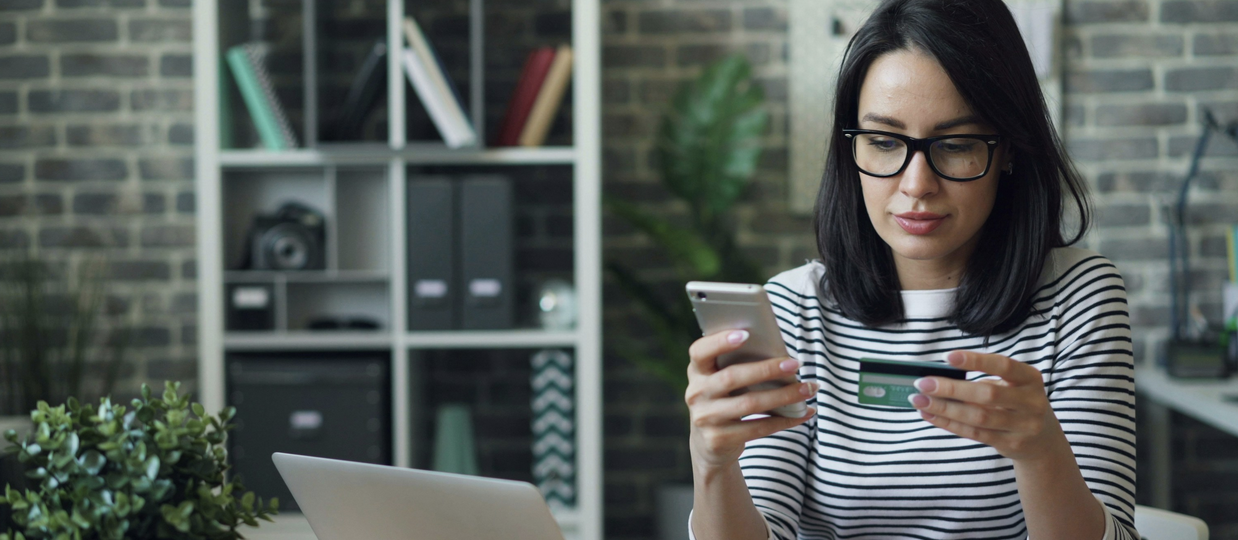 Woman reading credit card while holding phone and sitting in front of laptop